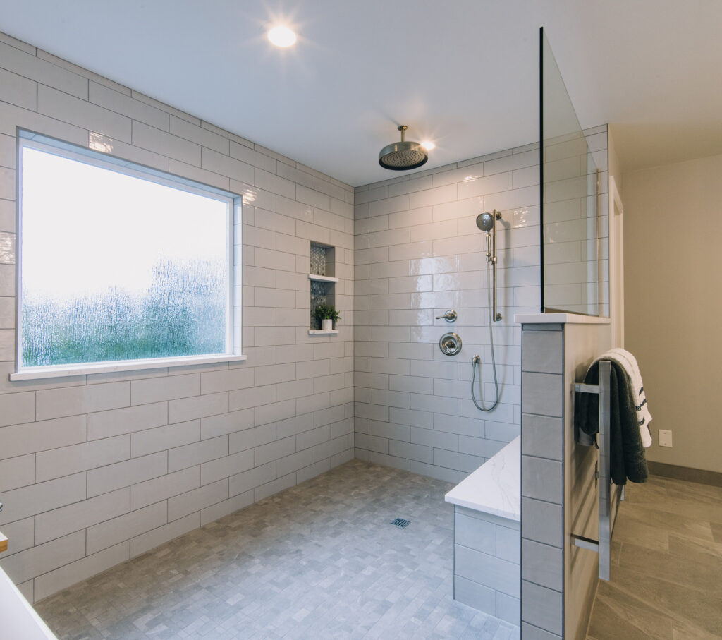 A Mill Creek bathroom remodel with A large wet room area featuring large grey tiles, a rain head shower fixture and a hand shower set. 