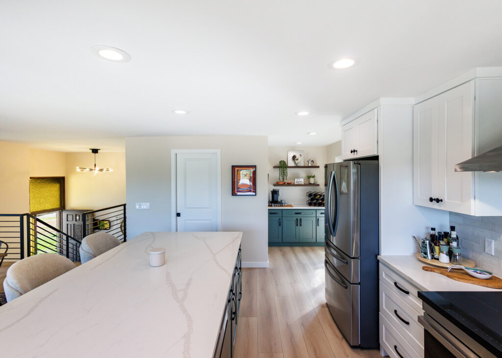 Custom kitchen and coffee bar by JL Remodeling with a quartz-topped island, green beverage-station cabinetry, walnut floating shelves, and a stainless steel refrigerator.
