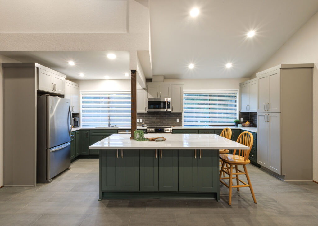 Remodeled kitchen in Everett, WA by JL Remodeling with green shaker cabinets, gray upper cabinetry, a green island with white quartz countertop and seating, and gray tile flooring.