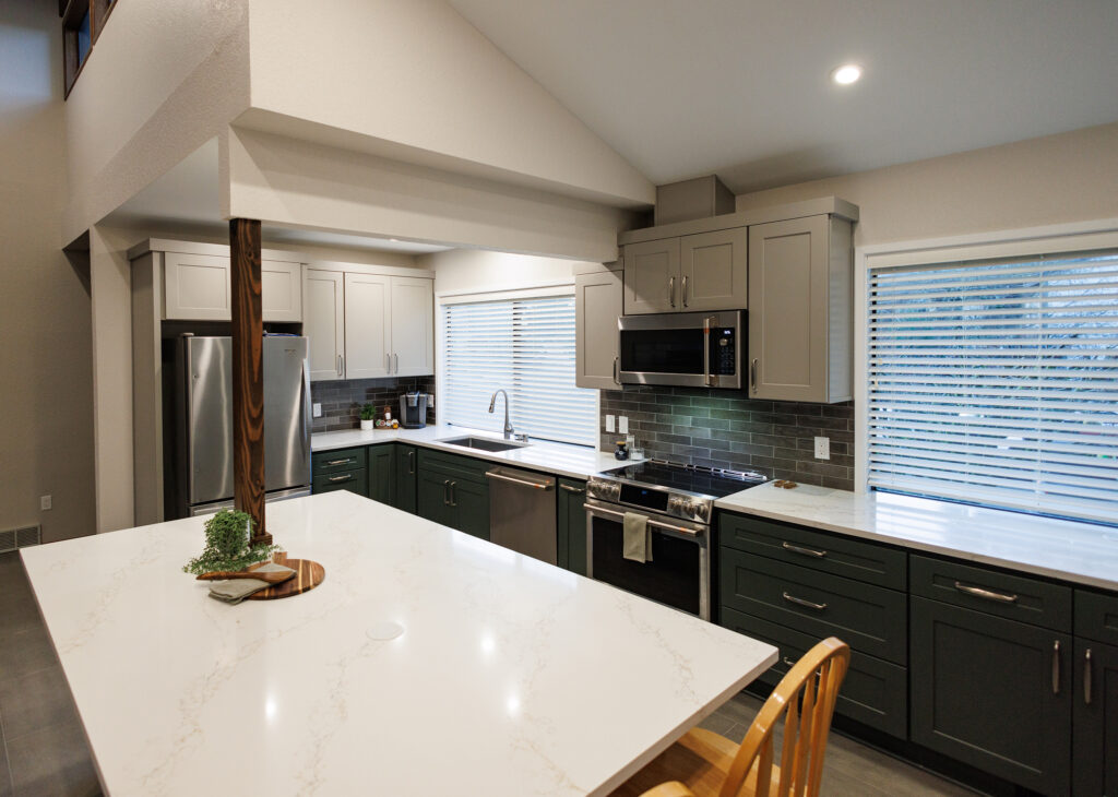 Everett, WA kitchen remodel with a vaulted ceiling, quartz-topped island, green and gray shaker cabinets, and stainless steel appliances beneath a sunlit window.