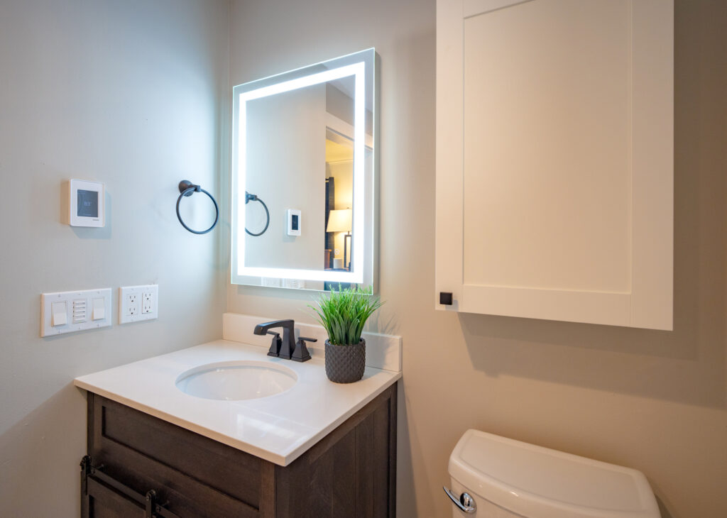 Remodeled bathroom in Everett, WA by JL Remodeling with a dark wood barn-door vanity, white quartz countertop, matte black faucet, and a backlit LED mirror.