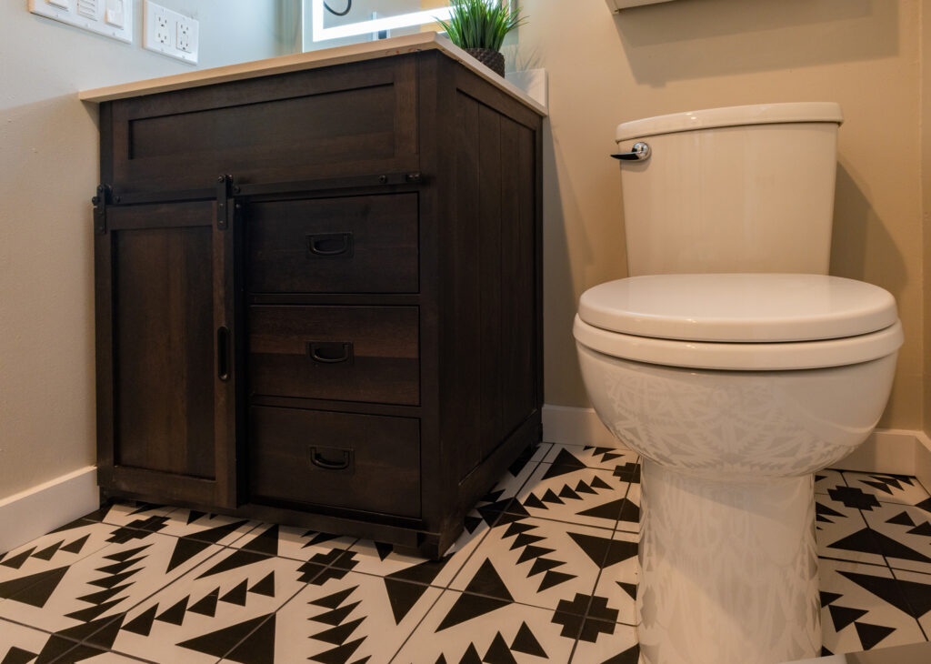 Craftsman-style bathroom vanity with a sliding barn door and dark wood drawers, paired with bold black-and-white geometric floor tile.
