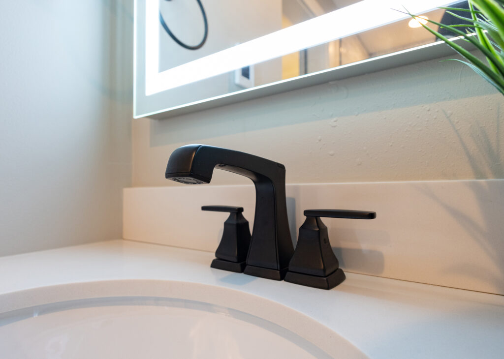 Matte black widespread faucet on a white quartz vanity beneath an LED mirror, a modern fixture detail from an Everett, WA bathroom remodel.