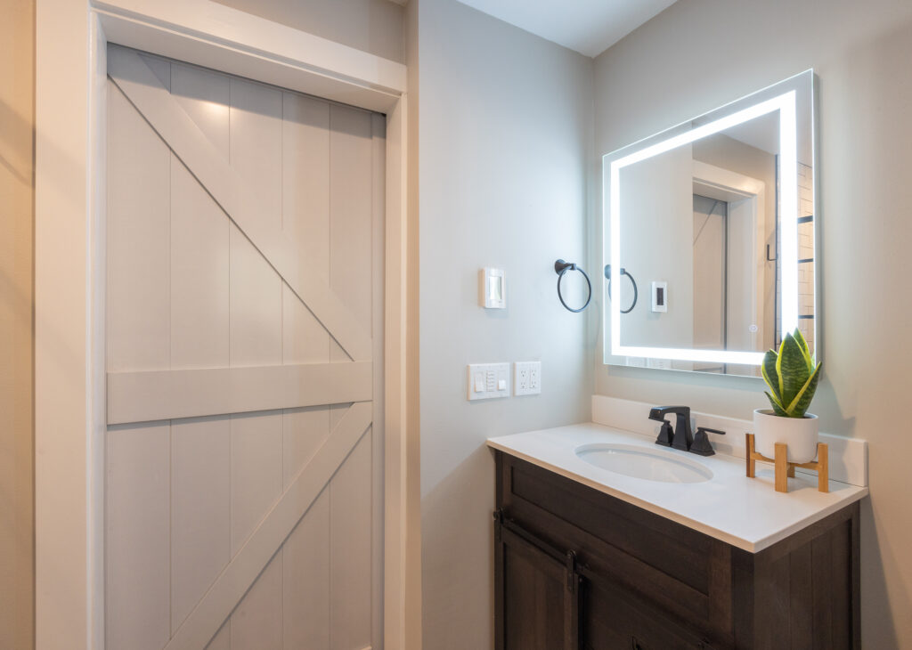 White sliding barn door beside a dark wood vanity, LED mirror, and matte black fixtures in a compact Everett, WA bathroom remodel.